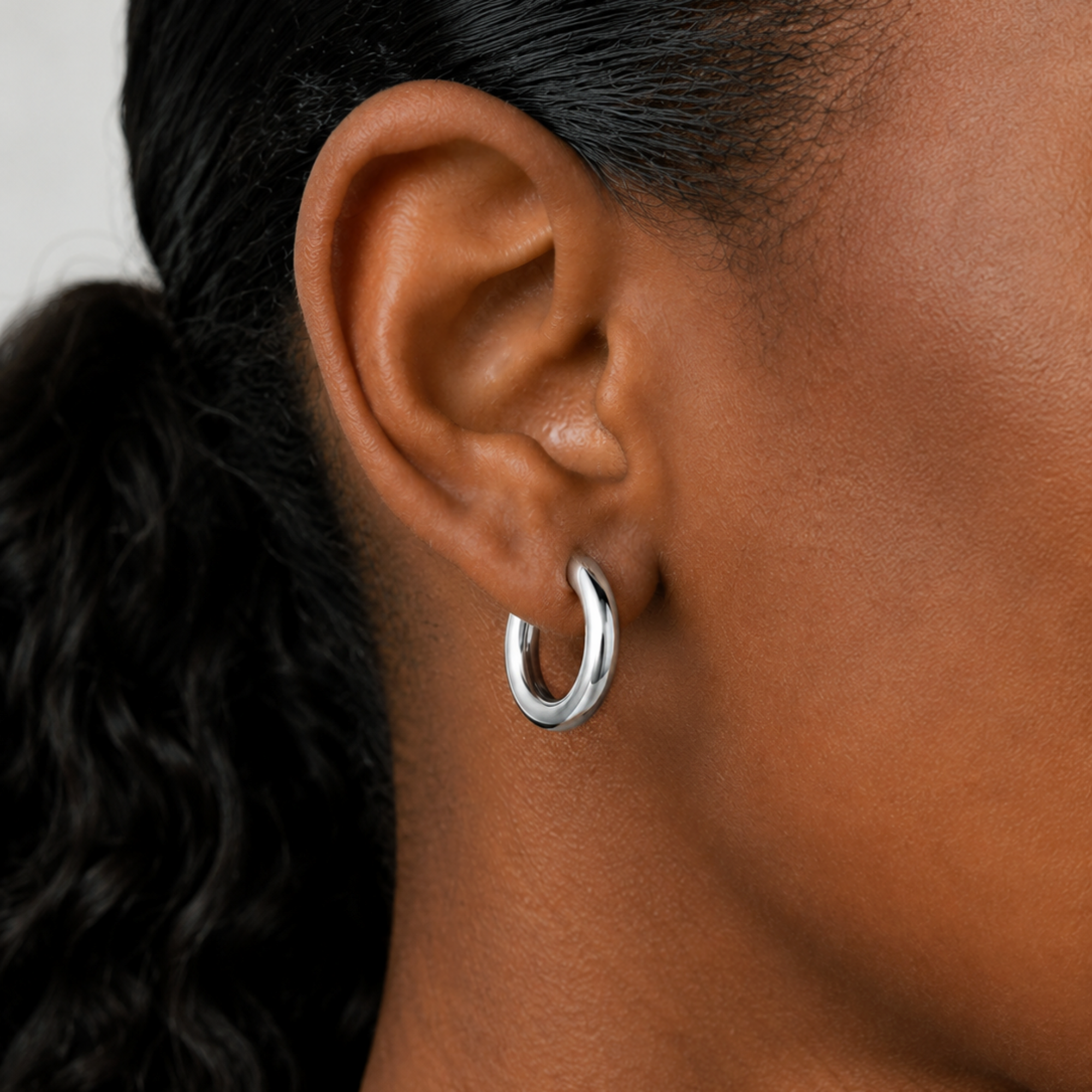Close-up of an ear wearing a silver hoop earring with blurred hair in the background