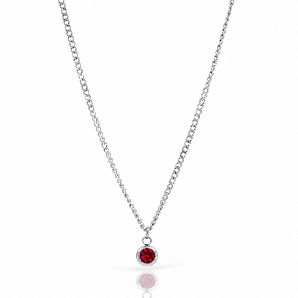 A silver chain necklace with a small round bezel pendant containing a deep red gemstone, displayed on a clean white background with a soft reflection below.
