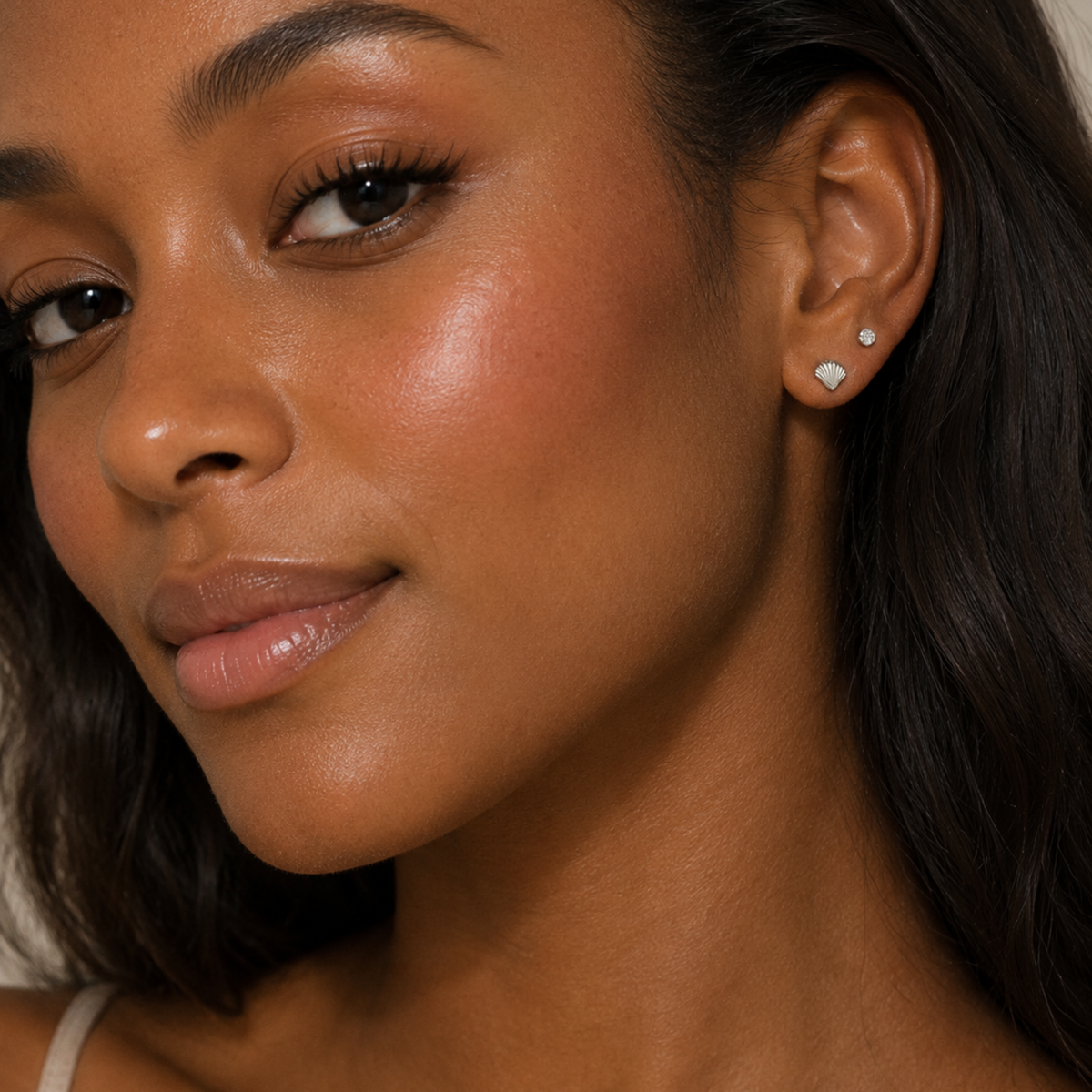 Close-up of a woman wearing small silver stud earrings, with one earring clearly showing a heart-shaped silver setting.