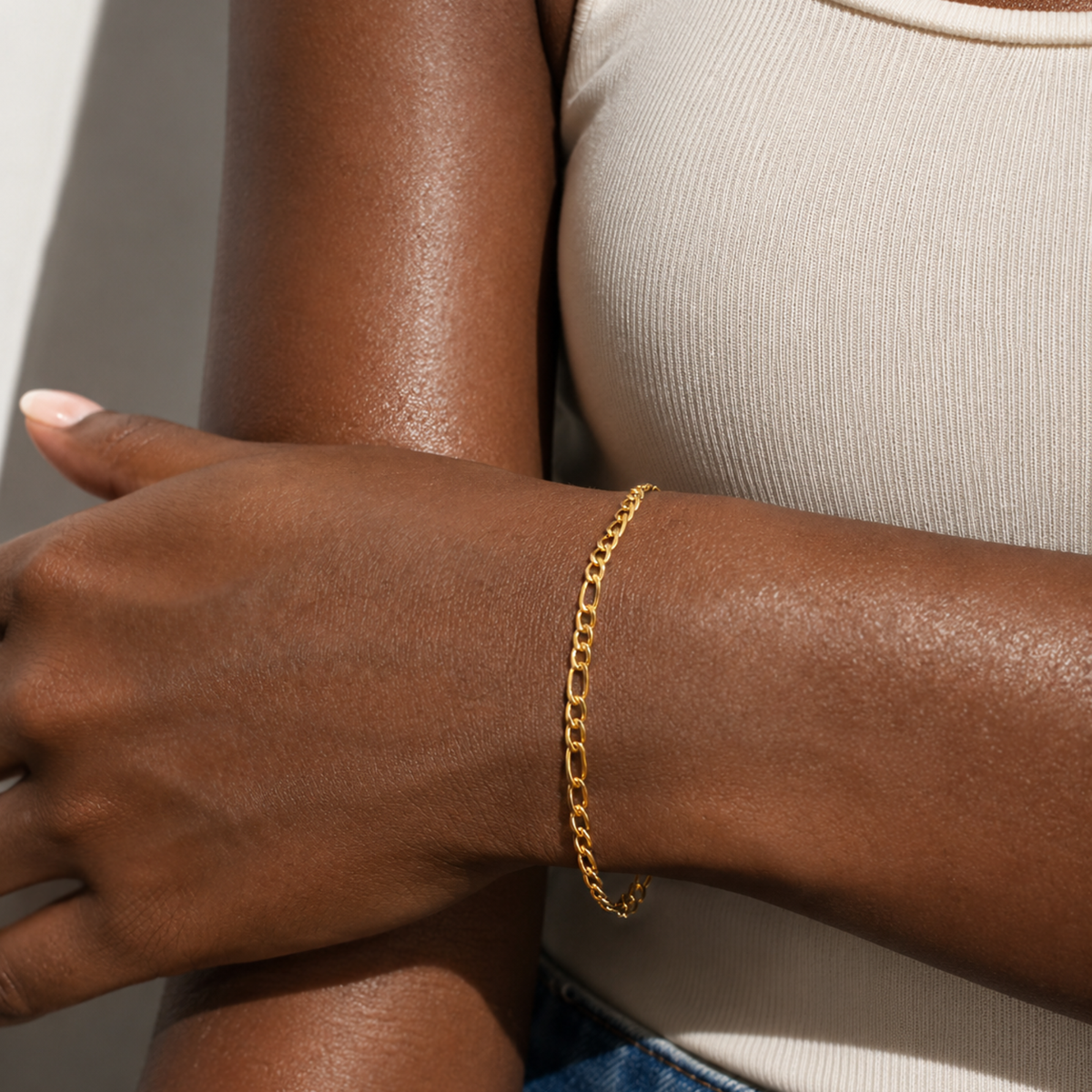 A close-up of a person's wrist wearing a delicate gold chain bracelet, paired with a ribbed beige top.